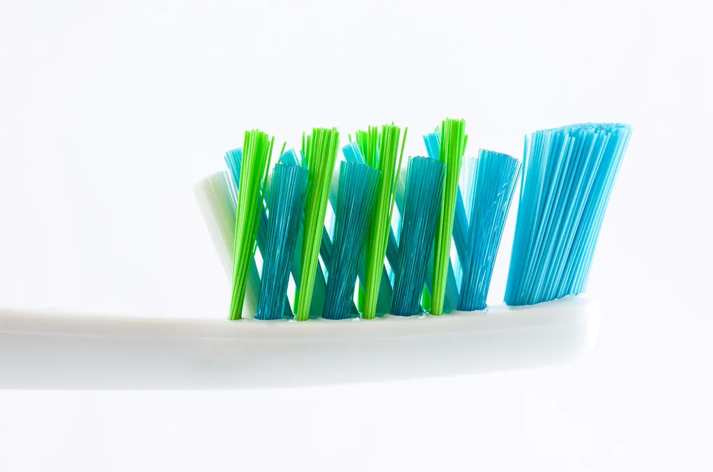 Cepillo de dientes con cerdas azules y verdes sobre fondo blanco