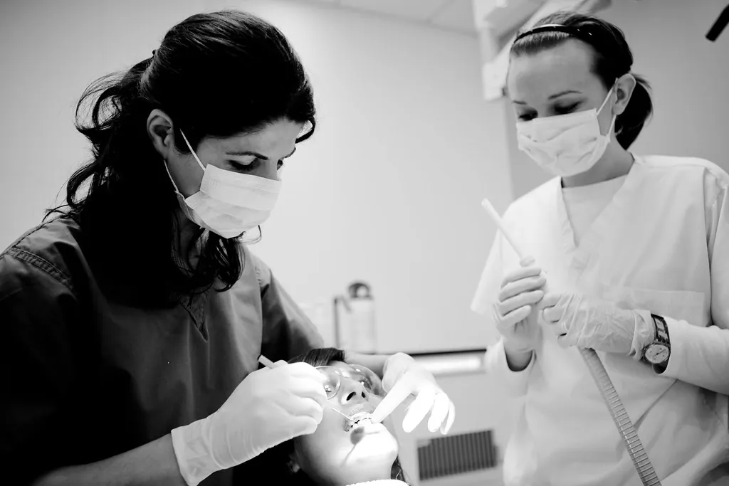 Dos profesionales con mascarilla atendiendo a un paciente, en blanco y negro